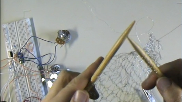 Image of the artists hands knitting silver wire with electronic components visible.